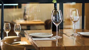 A dining table with wine glasses and a bottle of wine, set in a restaurant with a view through a window. - The Corner House (Seville)