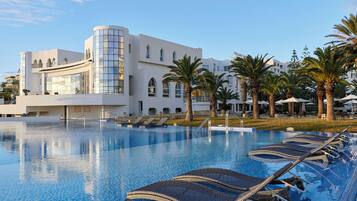A modern hotel with a swimming pool, palm trees, and lounge chairs.