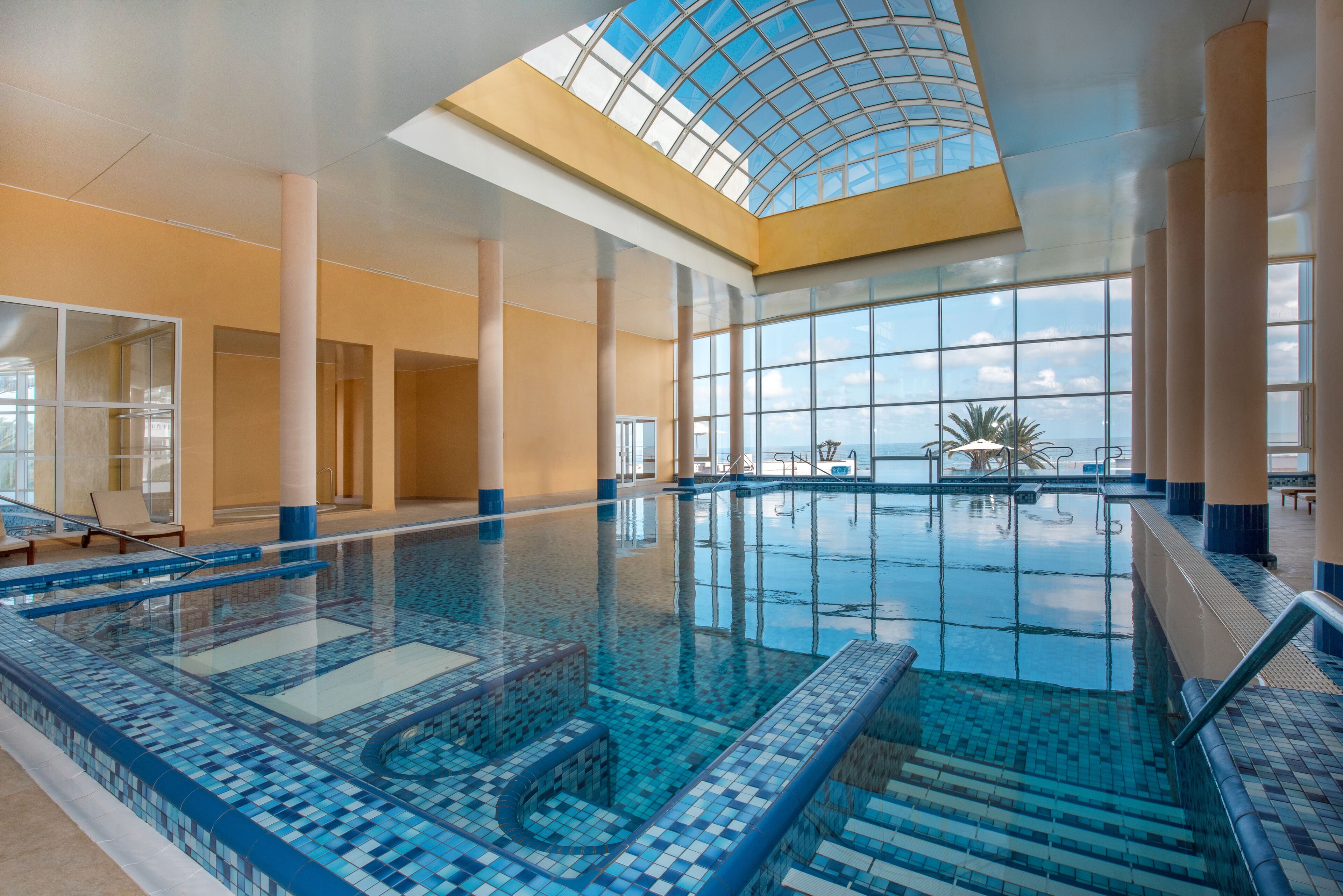 Una piscina interior con paredes de vidrio transparente, piso de baldosas y tragaluz.