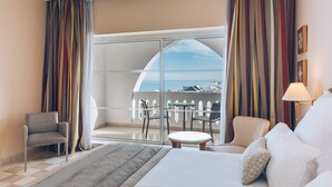 Habitación de hotel con cama, una silla, una mesita y un balcón con vistas.