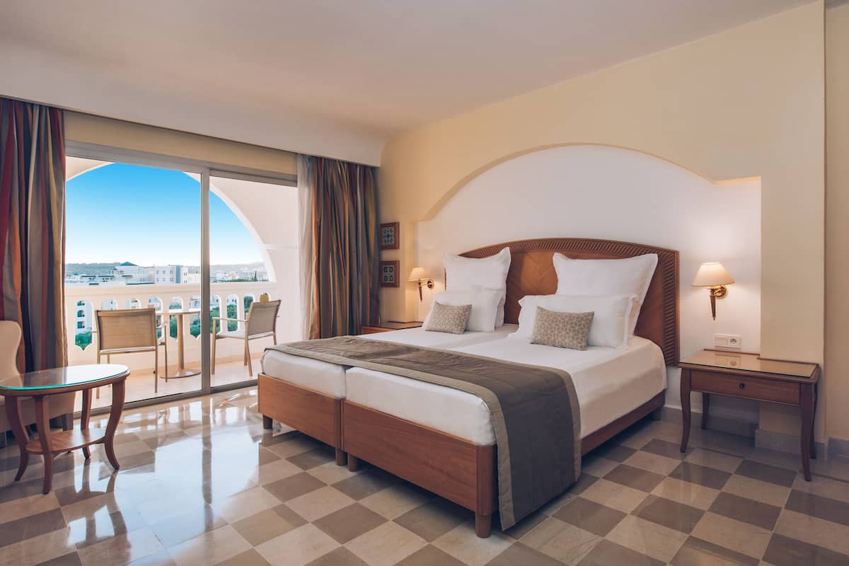 A hotel room with a large bed, a balcony with chairs, and a view of the city.