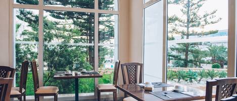 Un comedor con un gran ventanal arqueado, sillas de madera, una mesa con mantel individual y vistas a la vegetación.