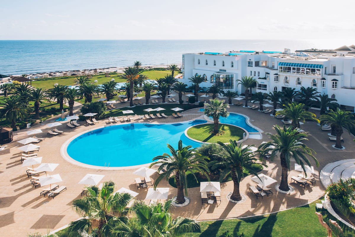 Un resort con una gran piscina, palmeras y vistas al océano.