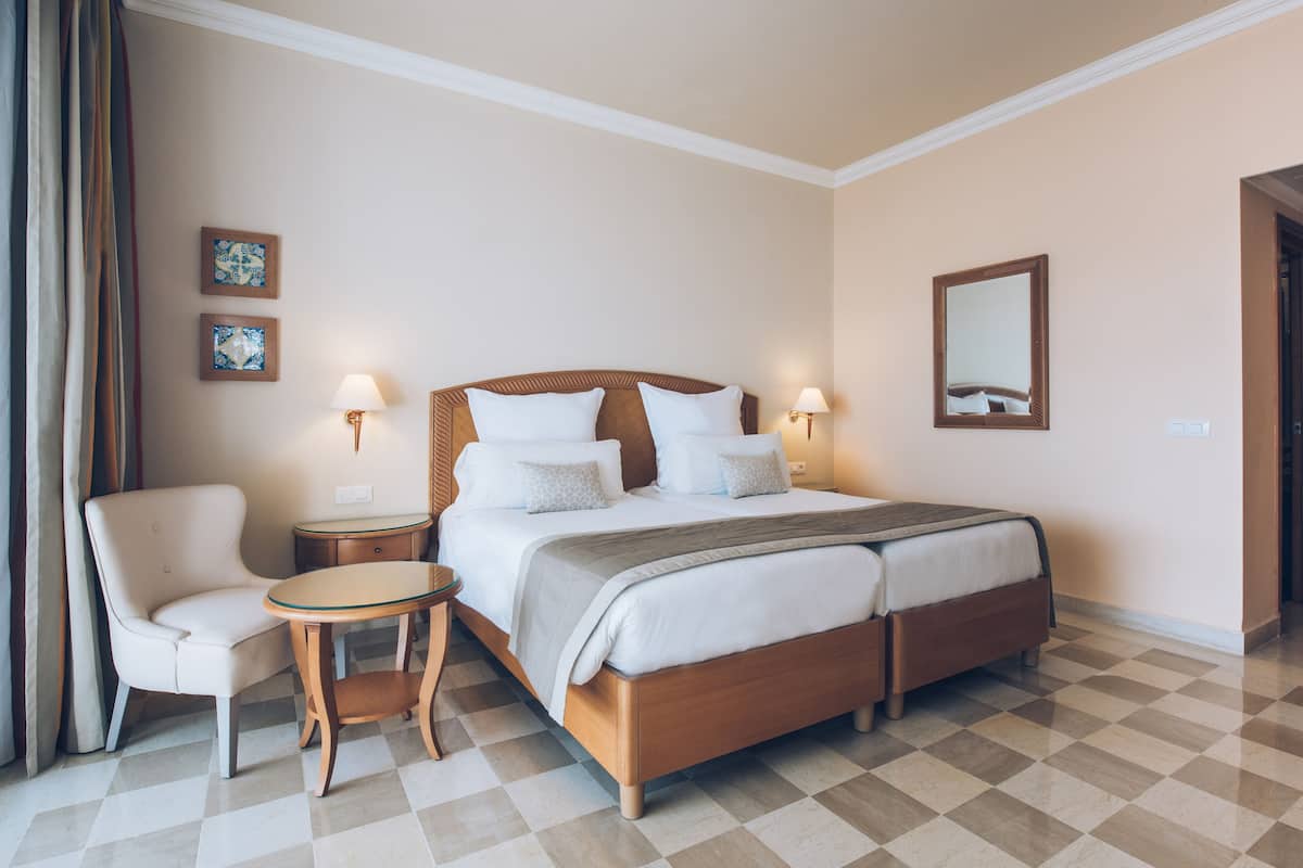 Habitación de hotel con una cama grande, una silla, una mesita y dos lámparas de pared.