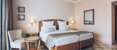 A hotel room with a large bed, a chair, a small table, and two wall-mounted lamps.