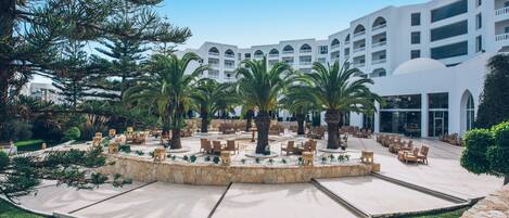 A hotel courtyard with outdoor seating, palm trees, and a white building with multiple balconies.