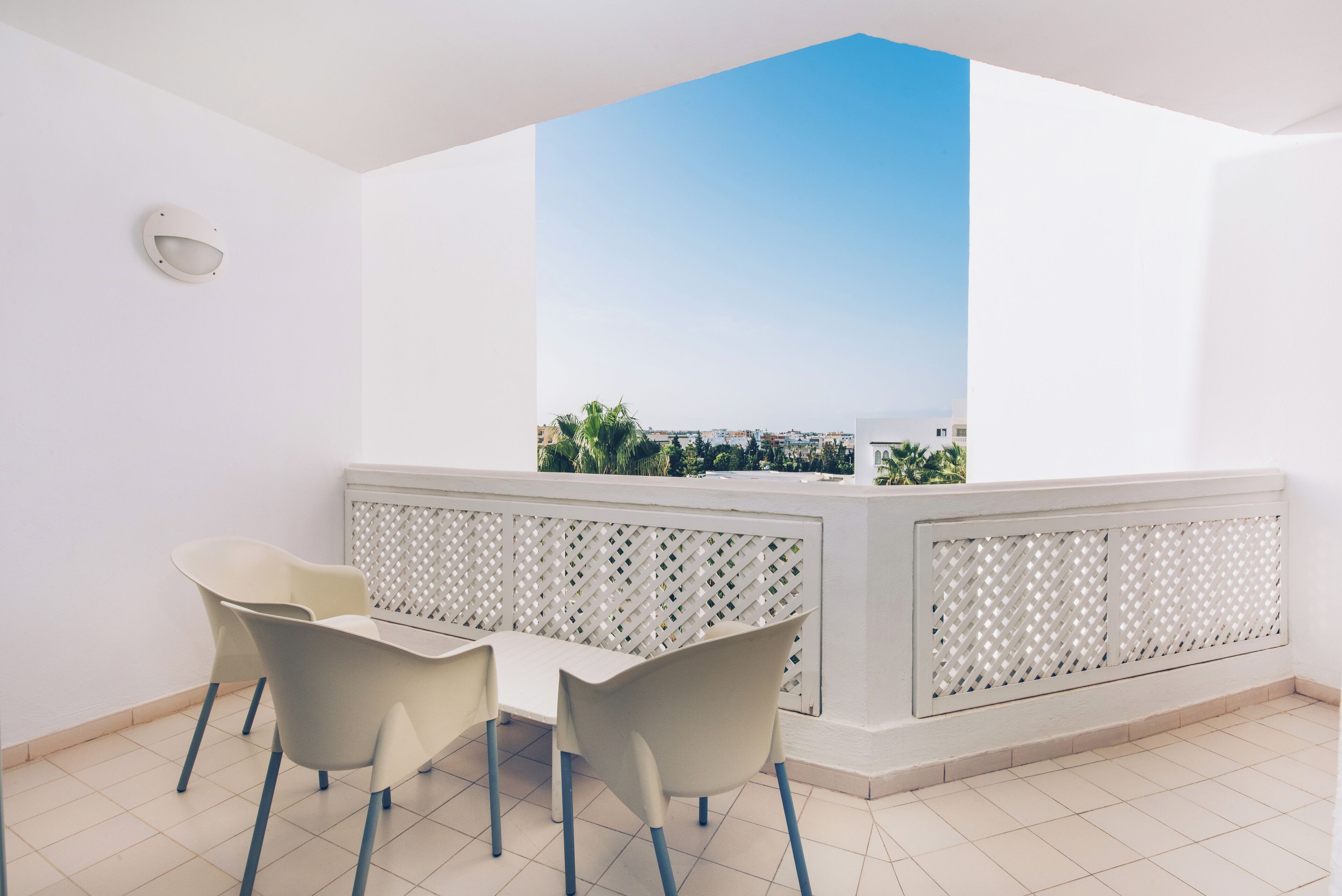 A balcony with a table and chairs, a white lattice partition, and a view of a cityscape.