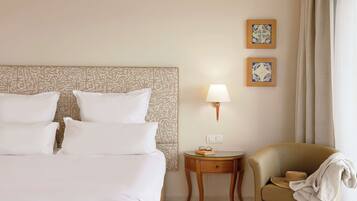 A hotel room with a large bed, a bedside table with a lamp, a chair, and two framed pictures on the wall.