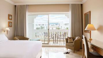 Quarto de hotel com cama, escrivaninha, cadeira, mesa e varanda com vista para edifícios.