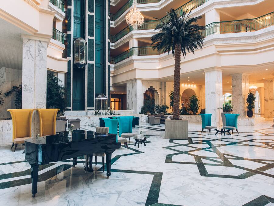 Un'ampia hall con un pianoforte a coda, diverse zone relax e una grande palma.