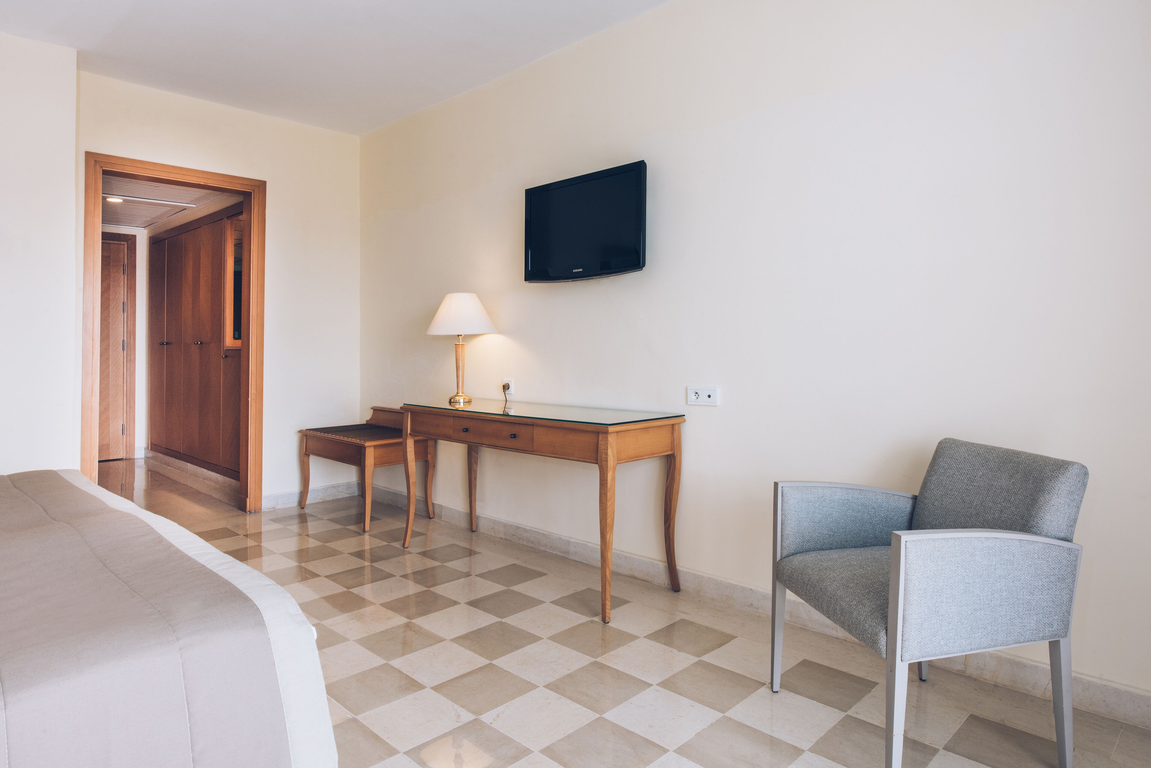A hotel room with a bed, a desk, a chair, a TV, and a lamp.