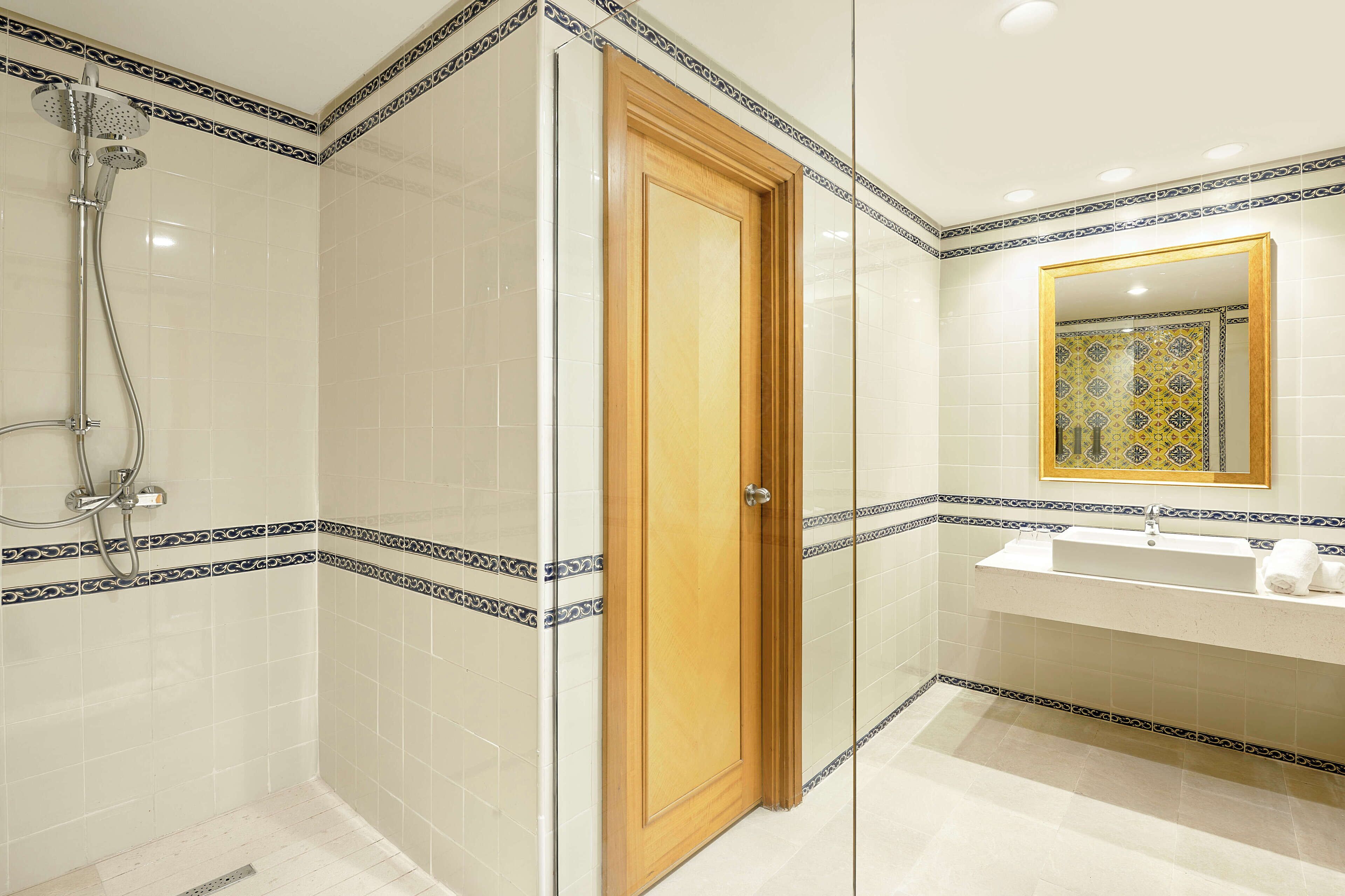 Un bagno con doccia vetrata, porta in legno, lavandino con specchio e piastrelle decorate.