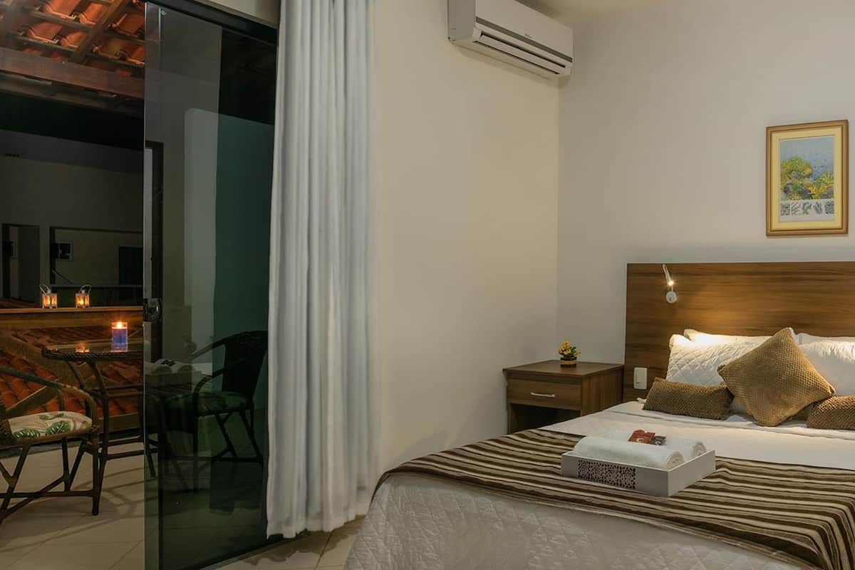 A hotel room with a bed, bedside tables, a small desk, a chair, and a balcony with a table and chairs.