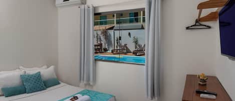 Una habitación de hotel con una cama, una ventana con cortinas, una mesita con un control remoto y un televisor en la pared.
