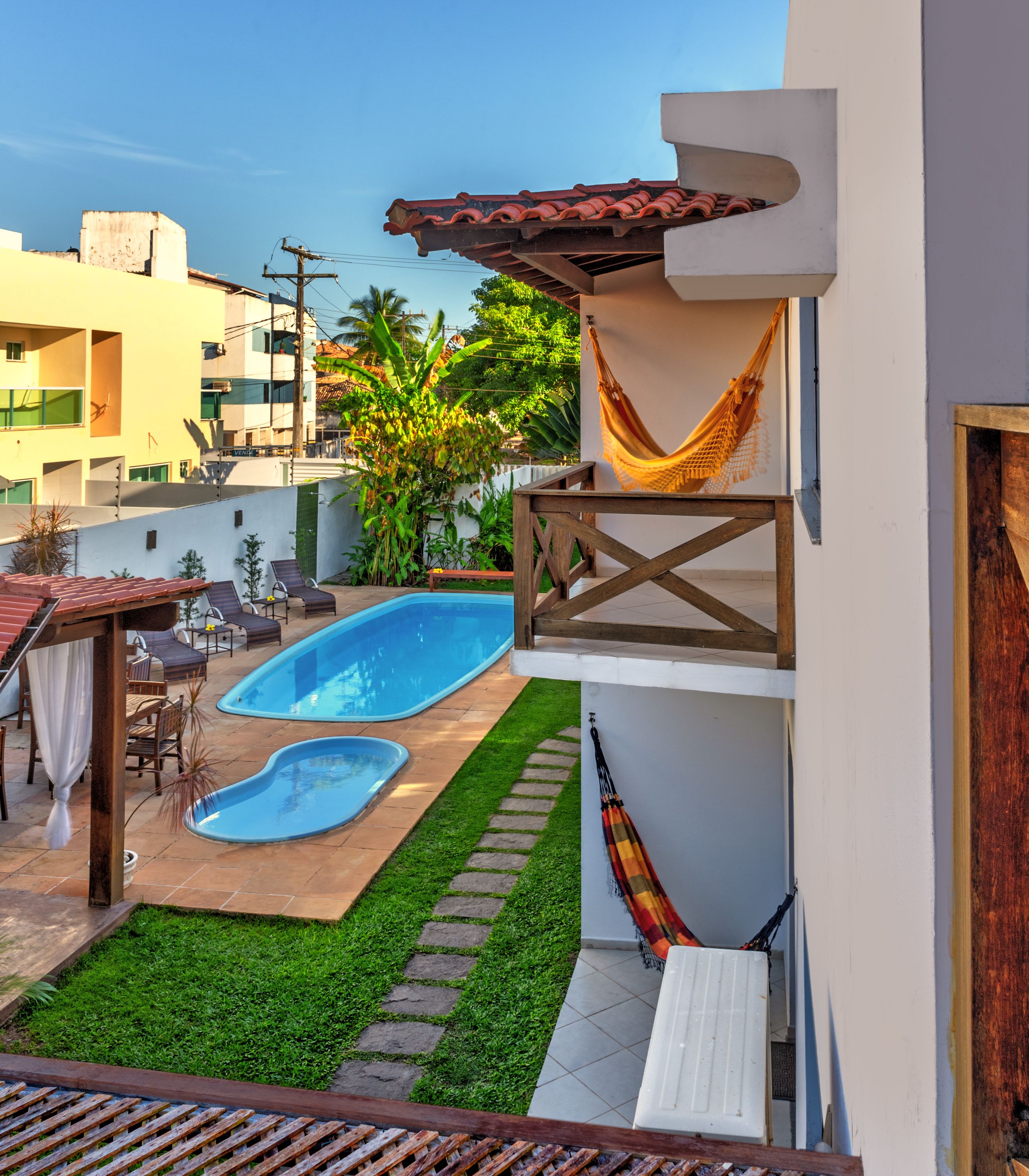 Un patio trasero con piscina, hamaca y un pequeño jardín.