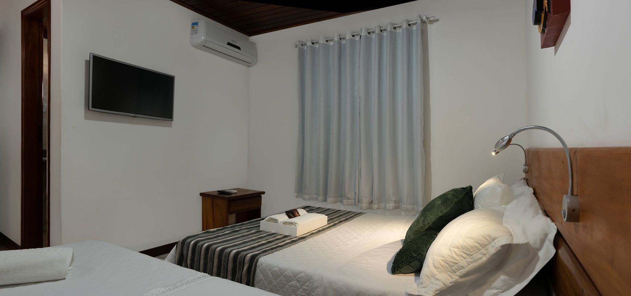 Een slaapkamer met een bed, nachtkastje en een aan de muur bevestigde televisie.