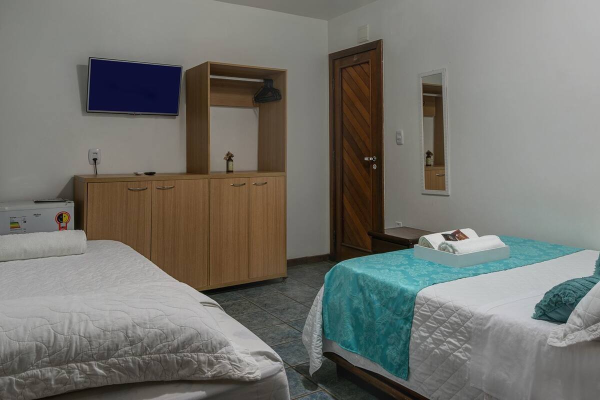 A hotel room with two beds, a wooden wardrobe, a television, and a mirror.