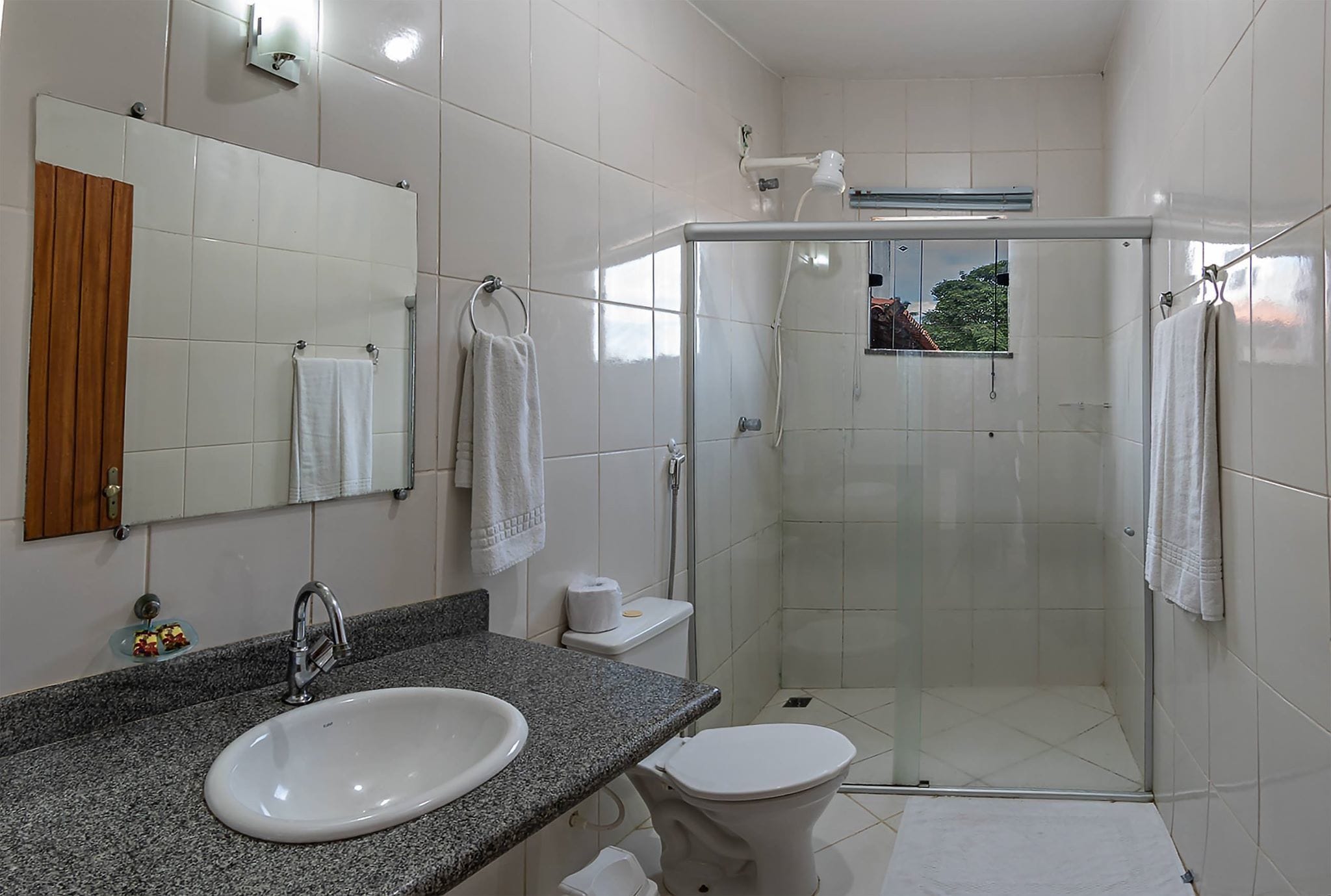 Un baño moderno con encimera de granito, un lavabo blanco, cabina de ducha con mampara de cristal y un inodoro.