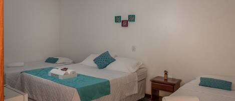 A hotel room with two beds, each with a white and teal bedspread, and a small bedside table with a lamp.