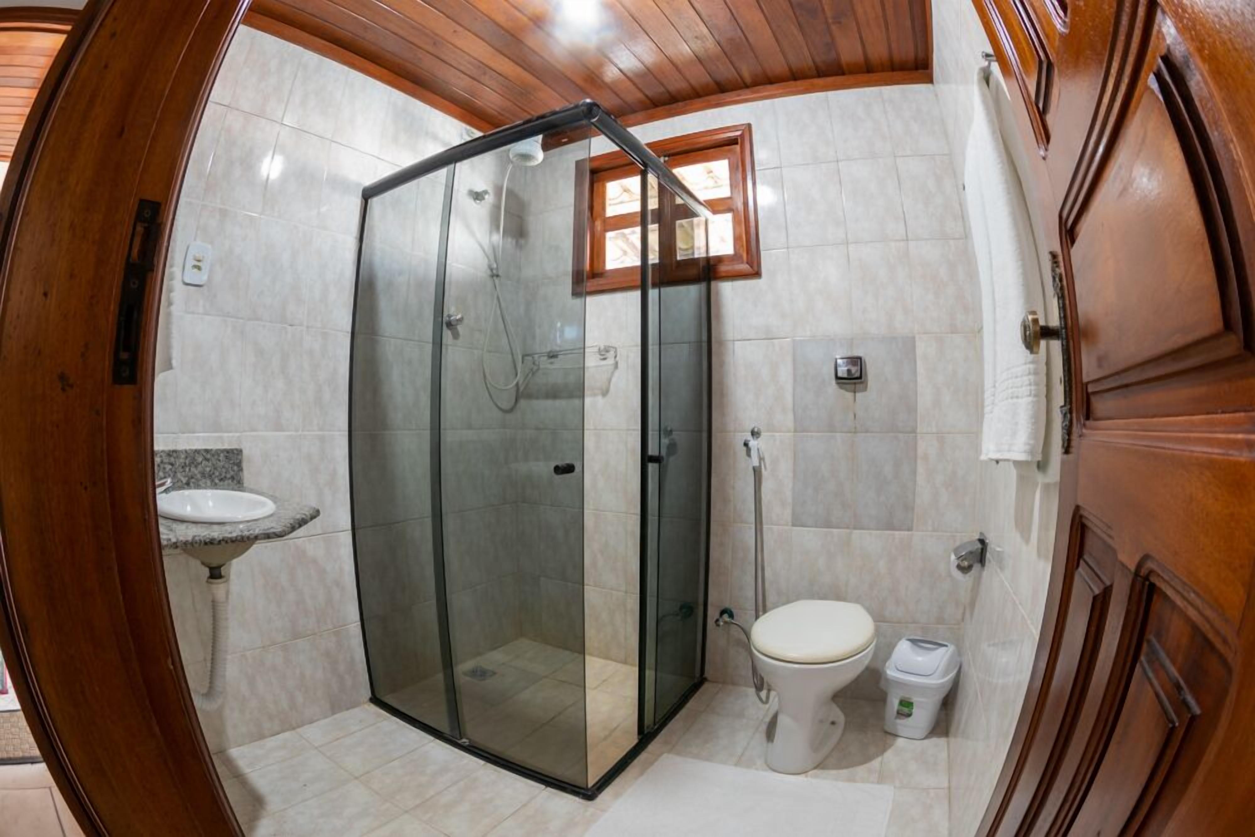 Bagno con doccia vetrata, lavandino, WC e mobili in legno.