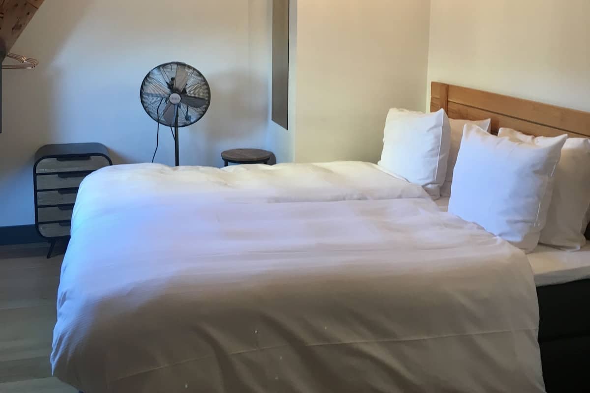 Een slaapkamer met een groot bed, een houten plafond en een staande ventilator.