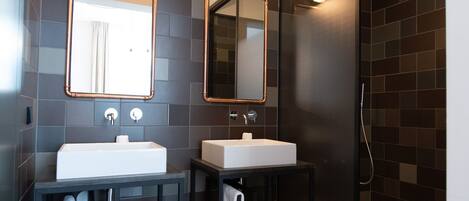A modern bathroom with two sinks, a glass shower enclosure, and a large mirror.