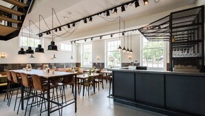 Ein modernes Restaurant mit einer zentralen Bar, verschiedenen Sitzbereichen und einer Treppe, die in eine obere Etage führt.