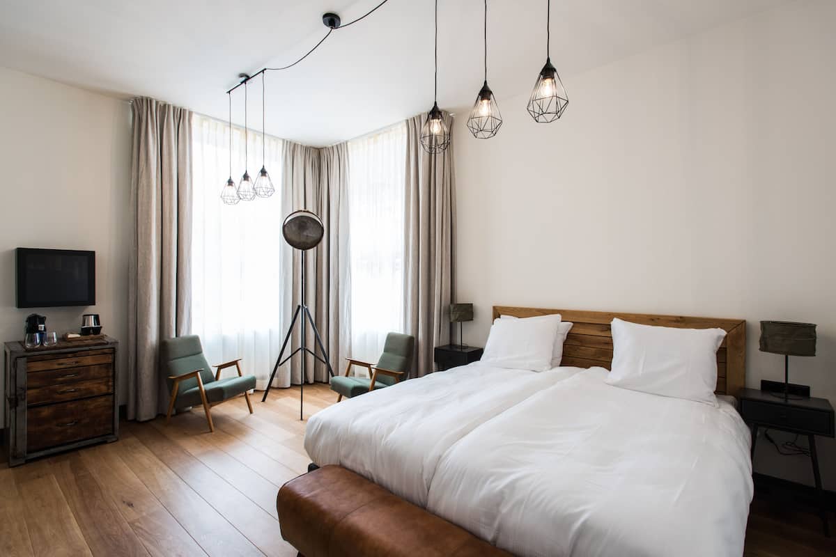 Een moderne hotelkamer met een groot bed, een bureau met een flatscreen televisie, een stoel, een lamp en uitzicht op het landschap door grote ramen.
