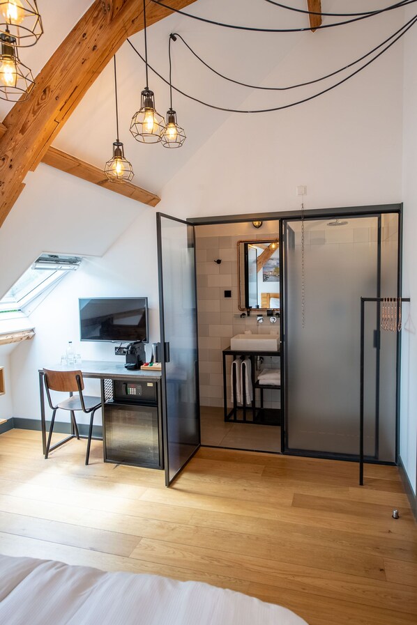 A modern bedroom with a wooden ceiling, a desk with a chair, a bed, and a bathroom with a sink and mirror. - Boutique Hotel d'Oude Morsch (Leiden)
