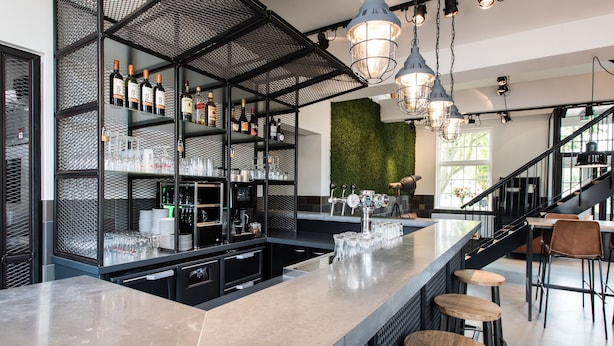 Eine moderne Bar mit Theke, Hockstühlen und Regalen voller Flaschen und Gläsern.