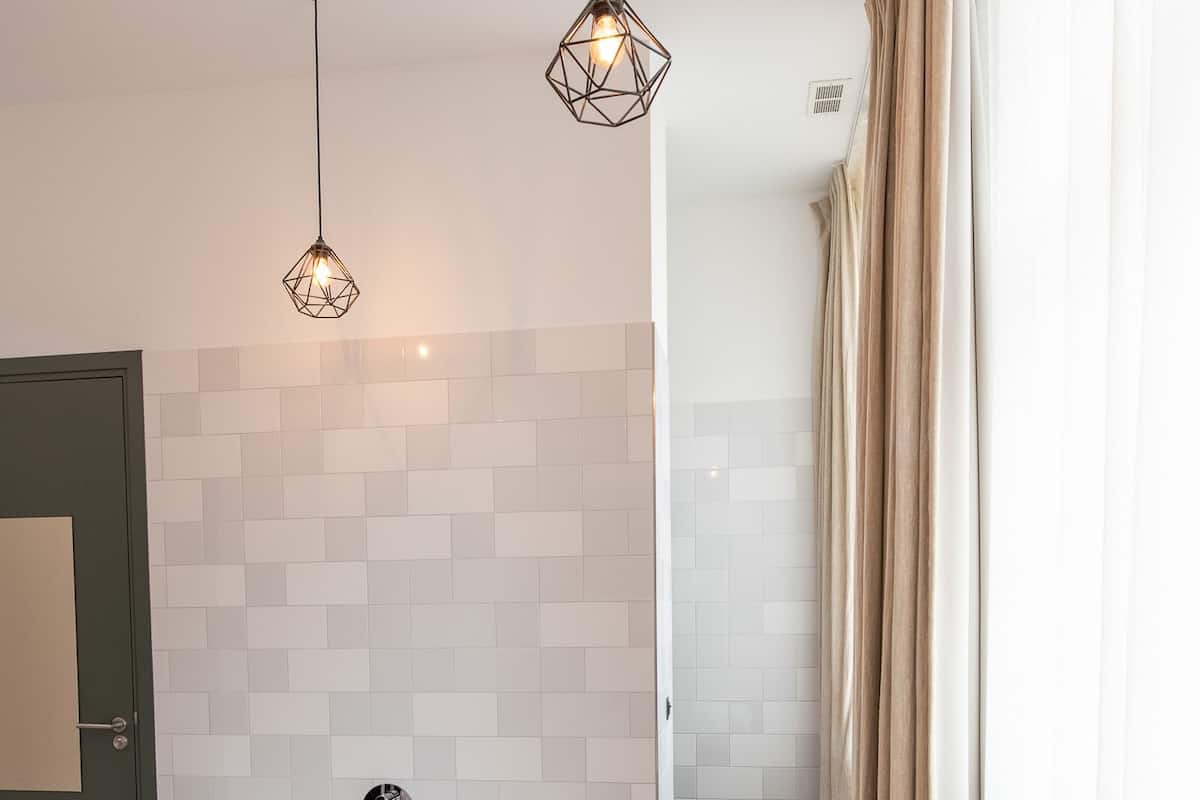 Een moderne badkamer met een vrijstaand bad, een houten vloer en een betegelde wand.