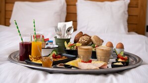Ein Frühstücksbrett mit verschiedenen Speisen und Getränken auf einem Bett mit weißer Bettwäsche und einem Holz-Kopfteil.