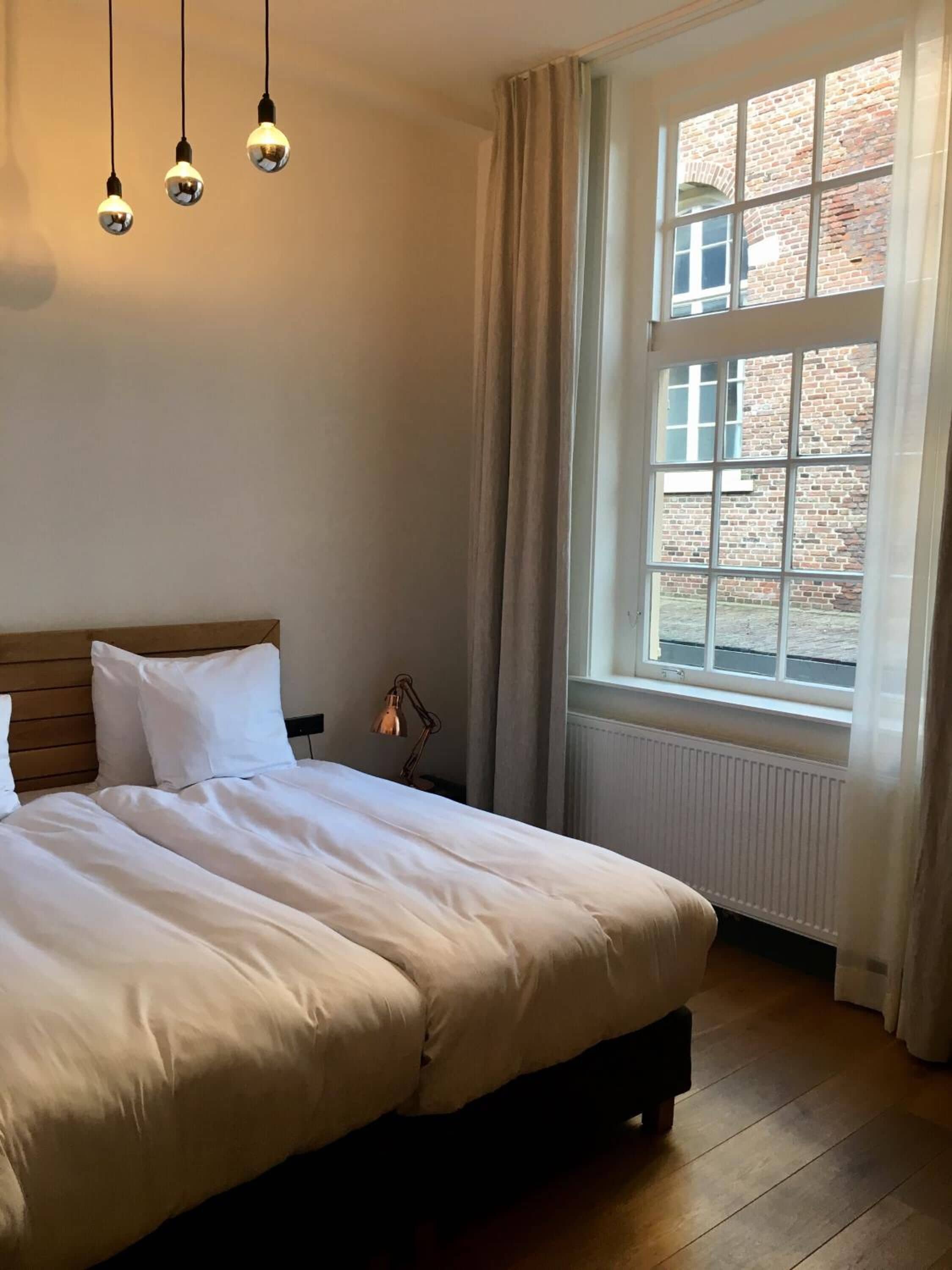 Ein Schlafzimmer mit einem großen Bett, einem Fenster mit Vorhängen und Pendelleuchten.