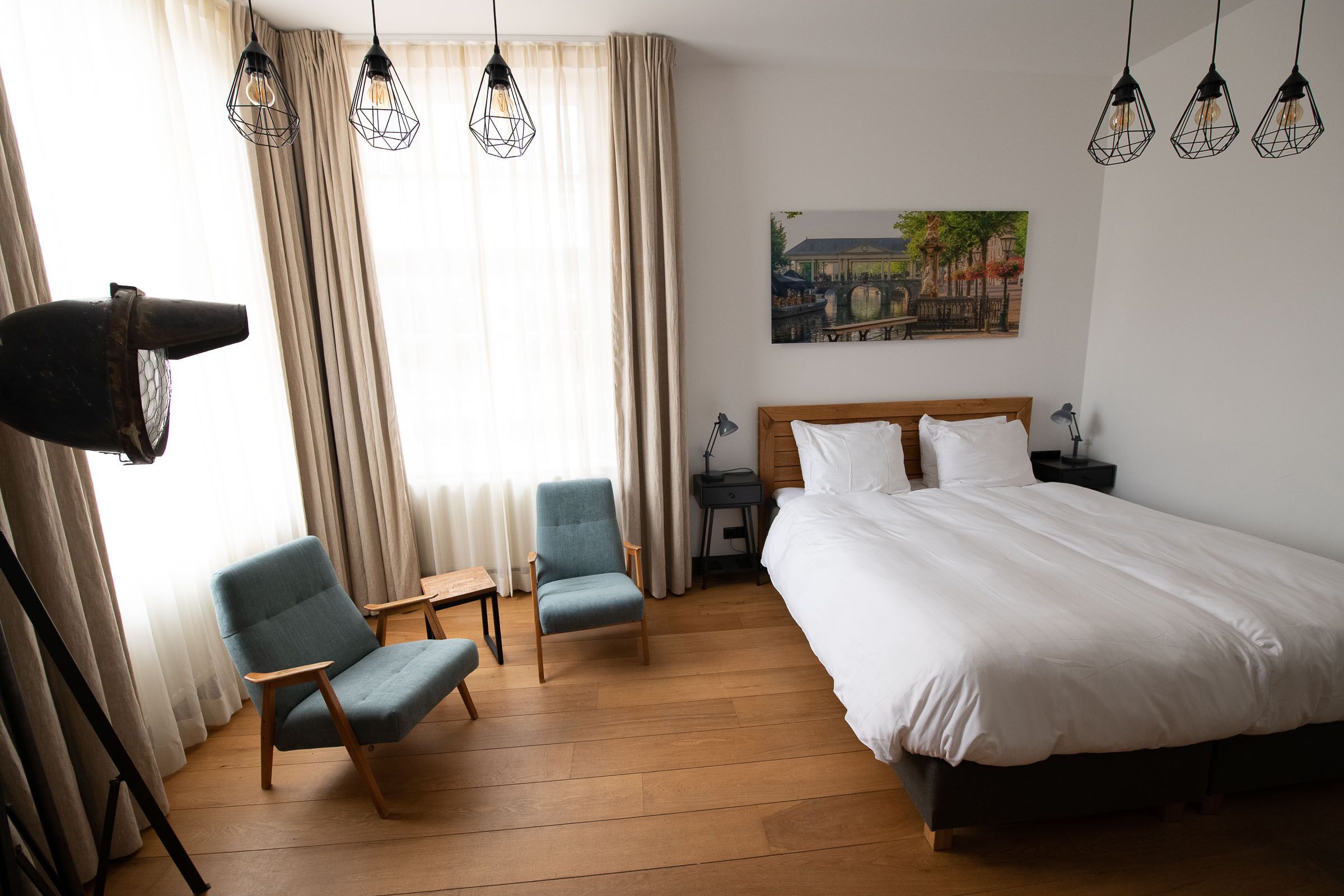 Habitación de hotel con una cama grande, dos sillones, un escritorio y un cuadro en la pared.