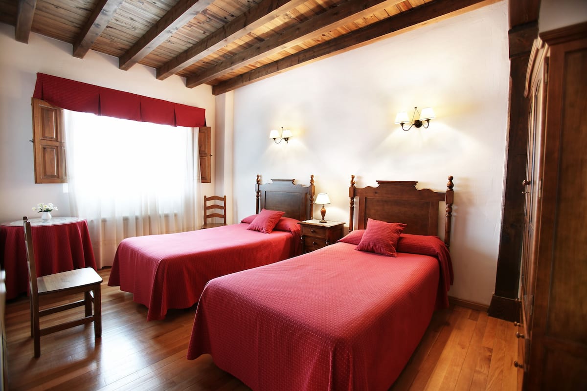 Ein Zimmer mit zwei Betten, Holzboden und einem mit Vorhängen versehenen Fenster.