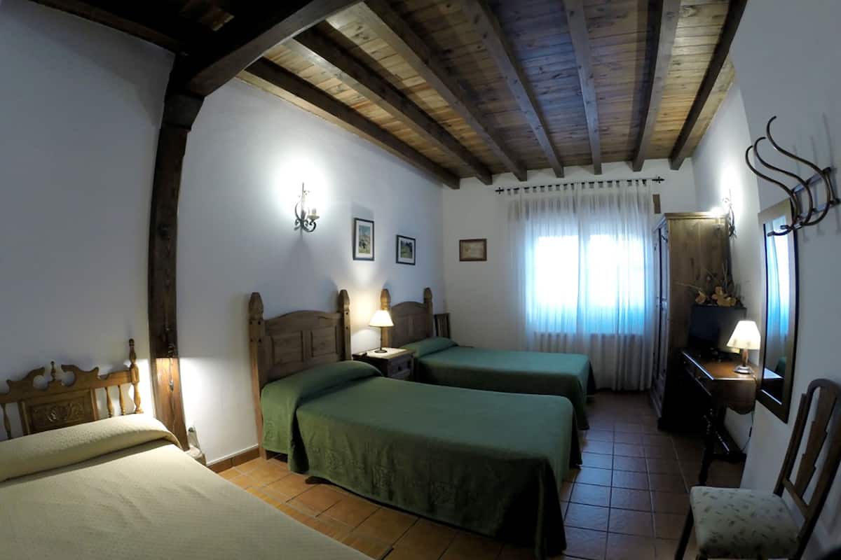 Ein Zimmer mit zwei Betten, Holzboden, einem Sessel, einem Schreibtisch mit Lampe und einem Spiegel.