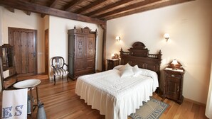 Un dormitorio con techo de madera, una cama grande con ropa de cama blanca, una mesita de noche de madera, una silla y un armario.