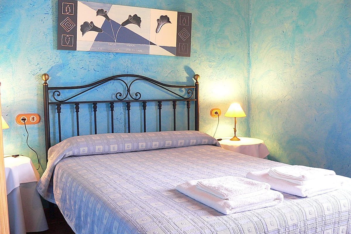 A bedroom with a bed, two bedside tables, a wall clock, and a framed picture.