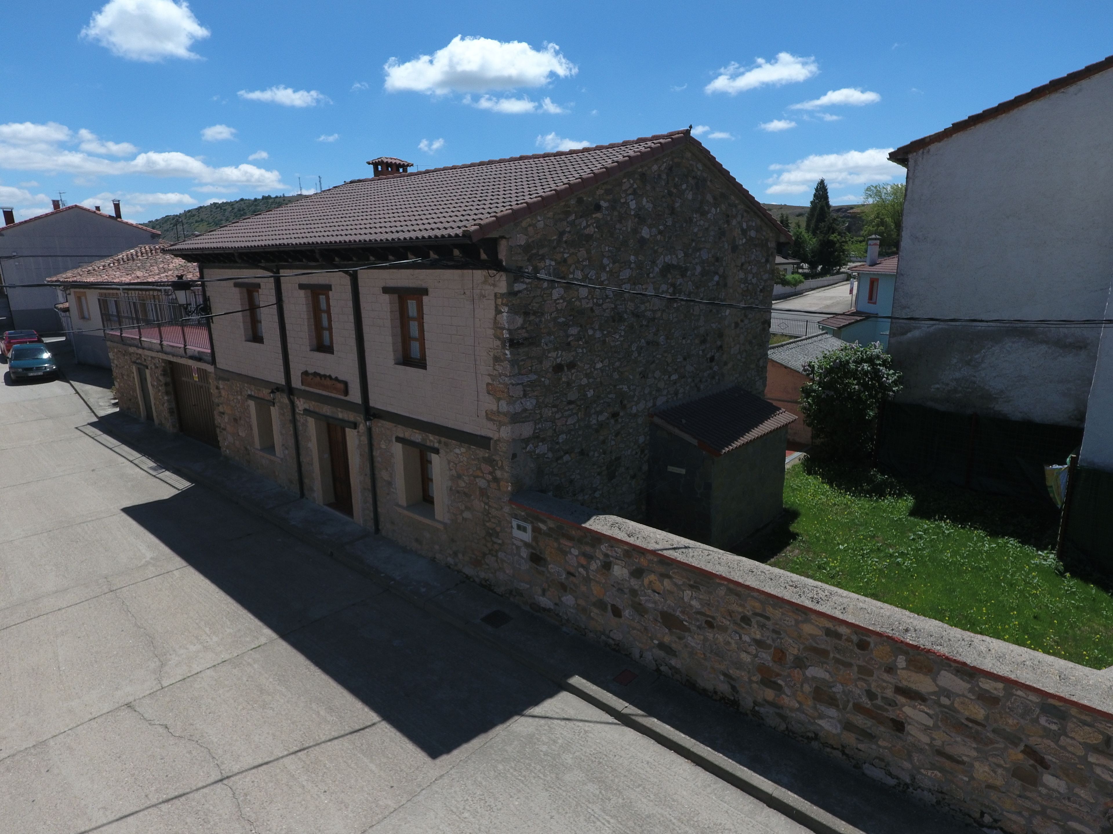 A two-story stone building with a tiled roof, a small attached structure, and a paved street in front.