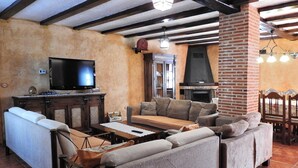 A cozy living room with a sofa, TV, fireplace, and wooden furniture. - Casa Rural La Majada Palentina (Santibanez de la Pena)