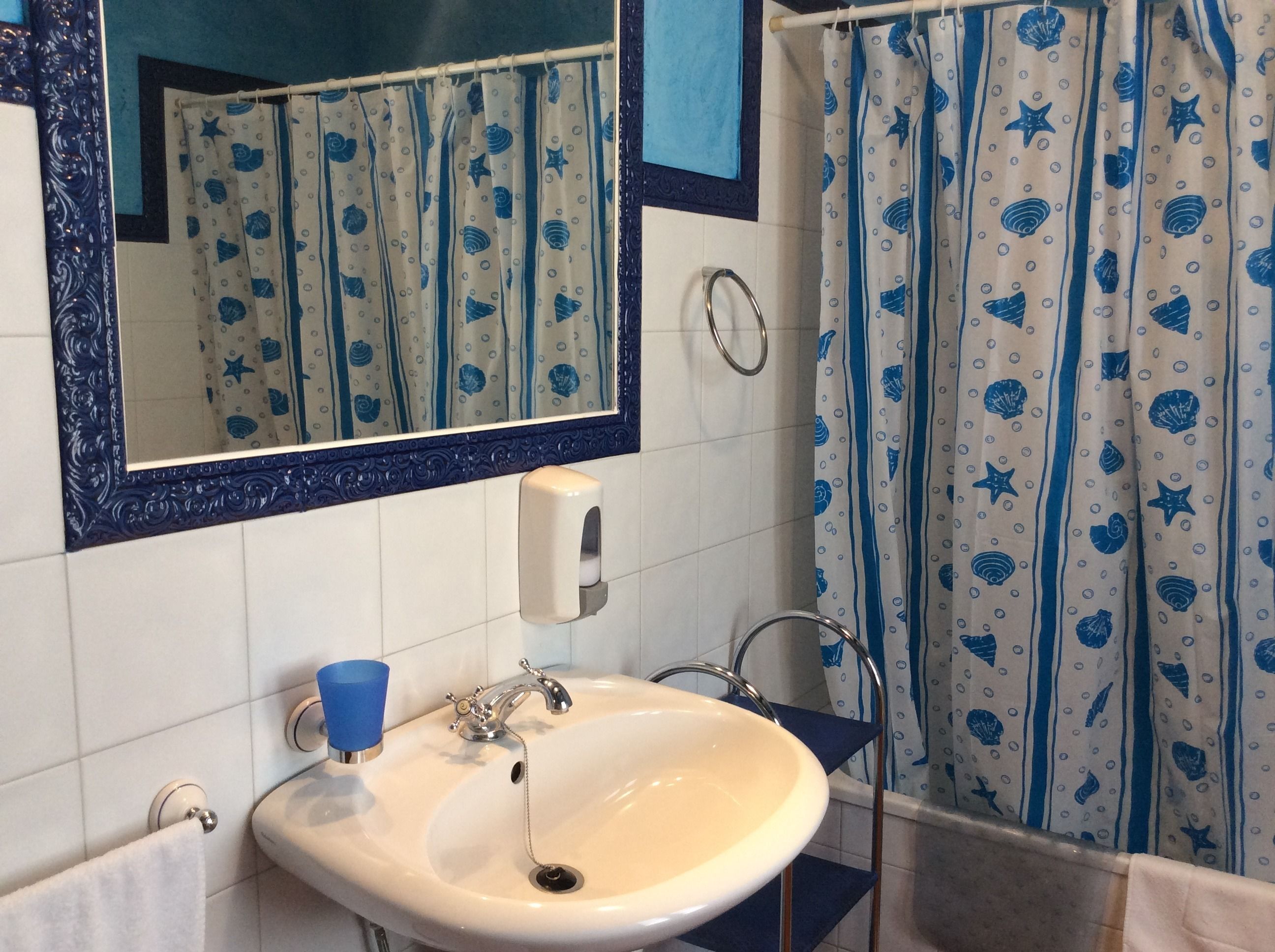A bathroom with a white sink, blue and white patterned shower curtain, and a mirror with a decorative frame.