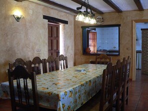 Una sala menjador amb una taula llarga, cadires de fusta i un mantell estampat.