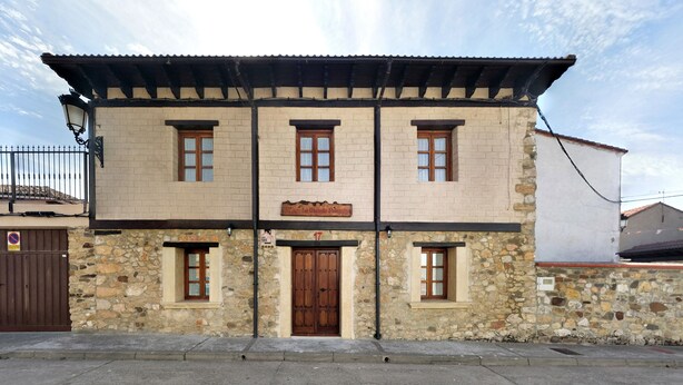 A two-story building with a stone facade, a central entrance with a wooden door, and multiple windows. - Casa Rural La Majada Palentina (Santibanez de la Pena)