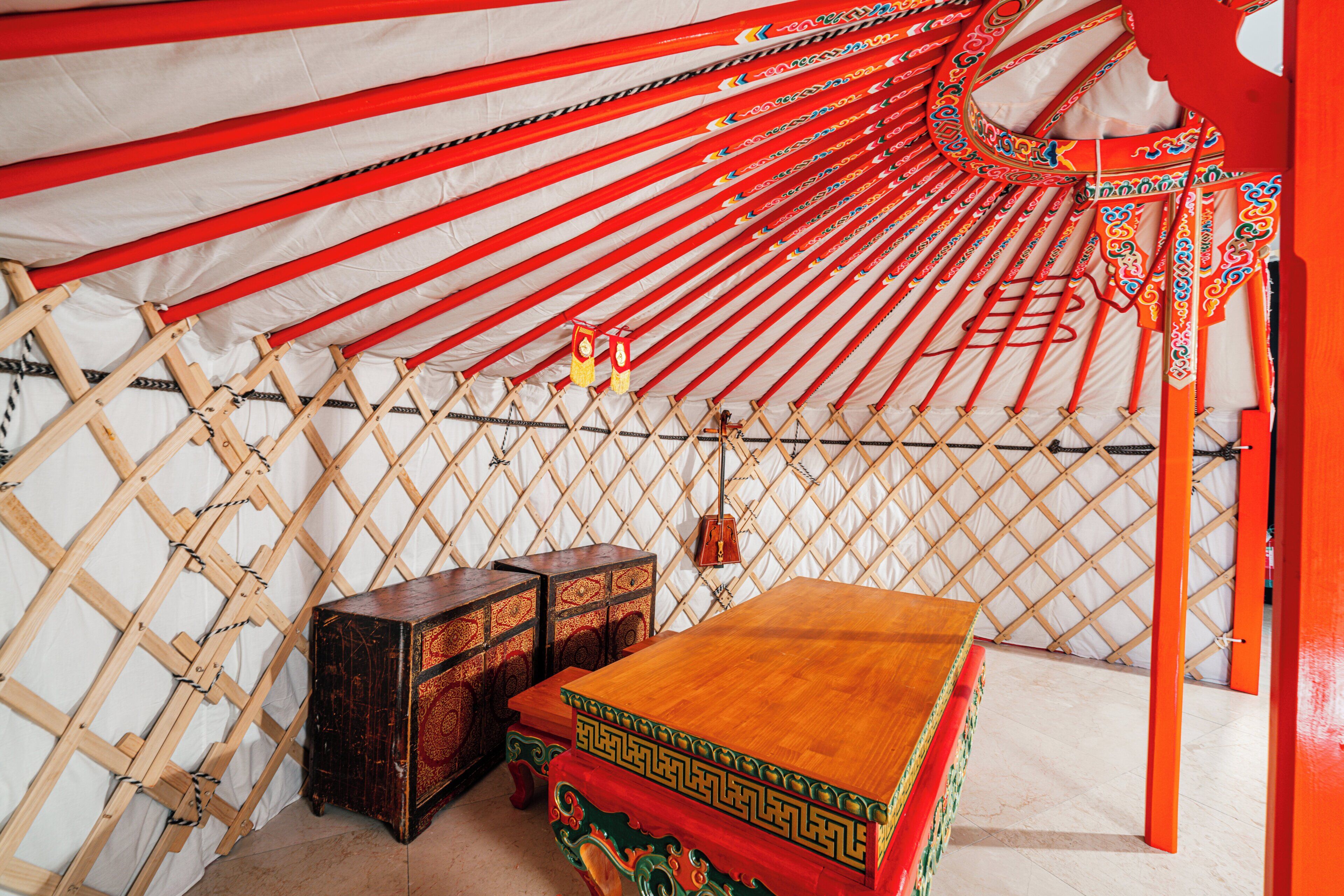 Interior de una yurta tradicional con una mesa de madera, dos cajas de almacenamiento y un adorno colgante.