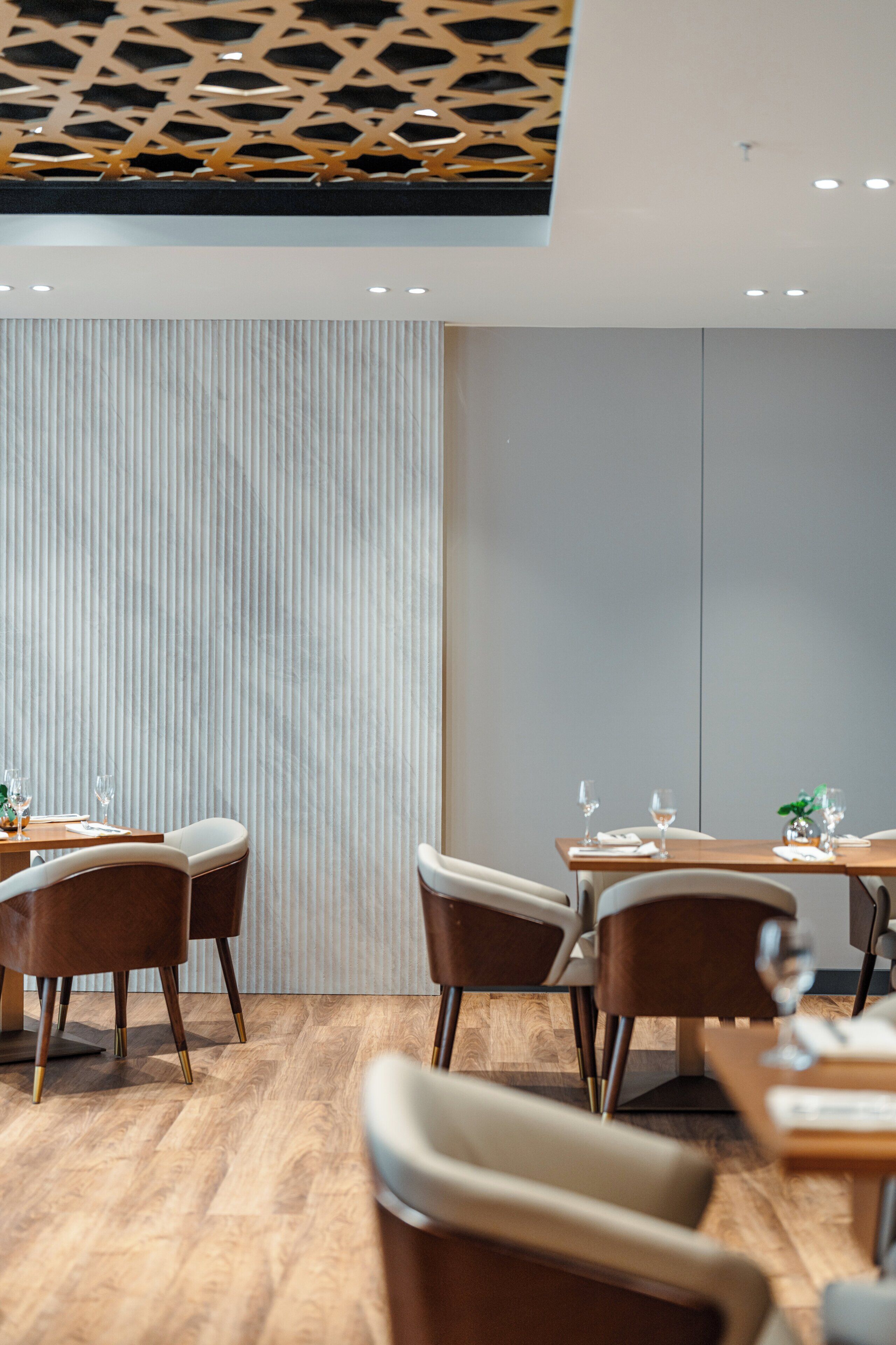 A modern dining area with wooden tables and chairs, a patterned ceiling, and a vertical striped wall.