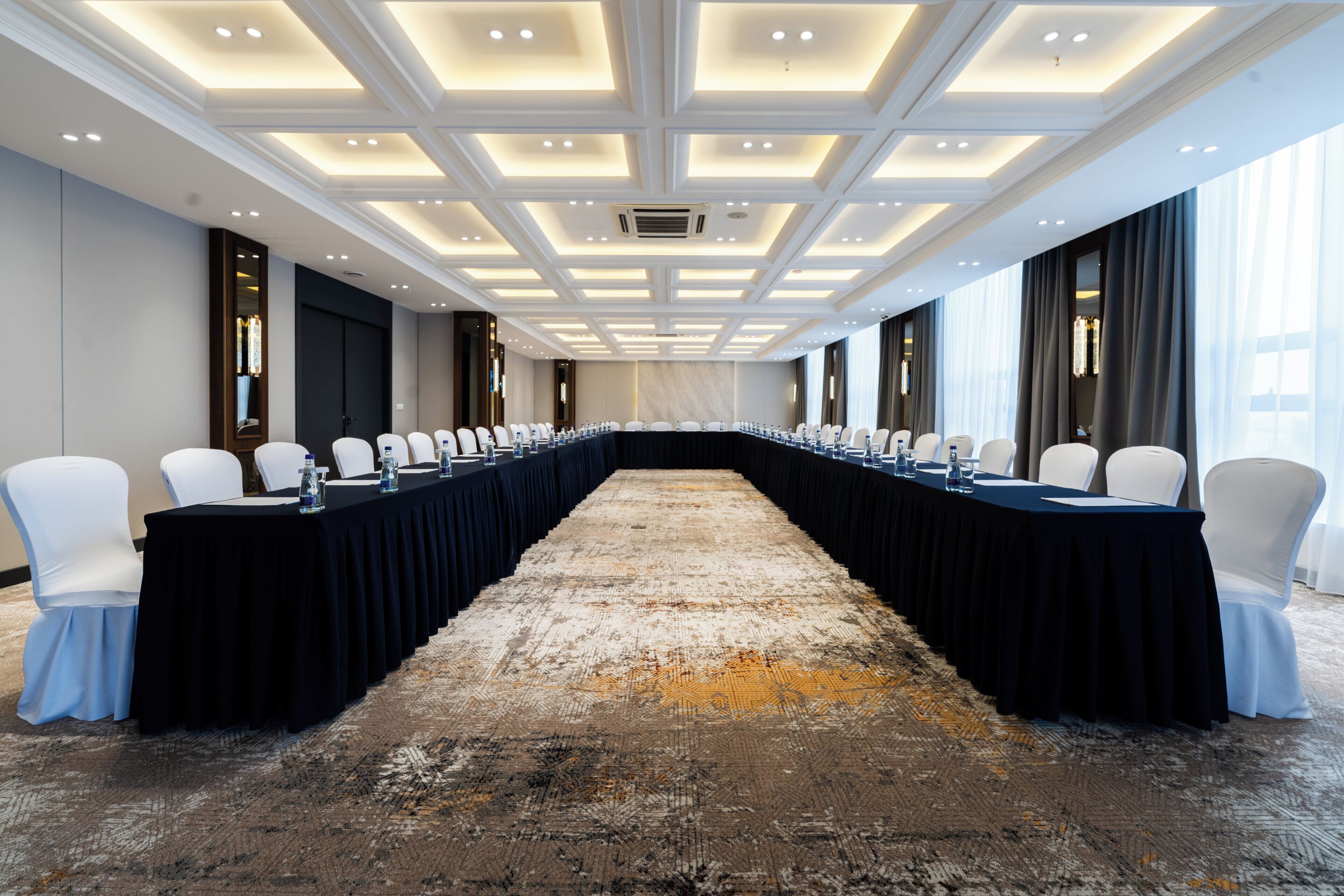 Une salle de conférence avec une longue table, des chaises blanches et un sol recouvert de moquette.