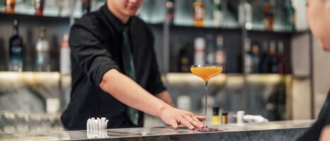 A bartender preparing a drink at a bar with a variety of bottles in the background.