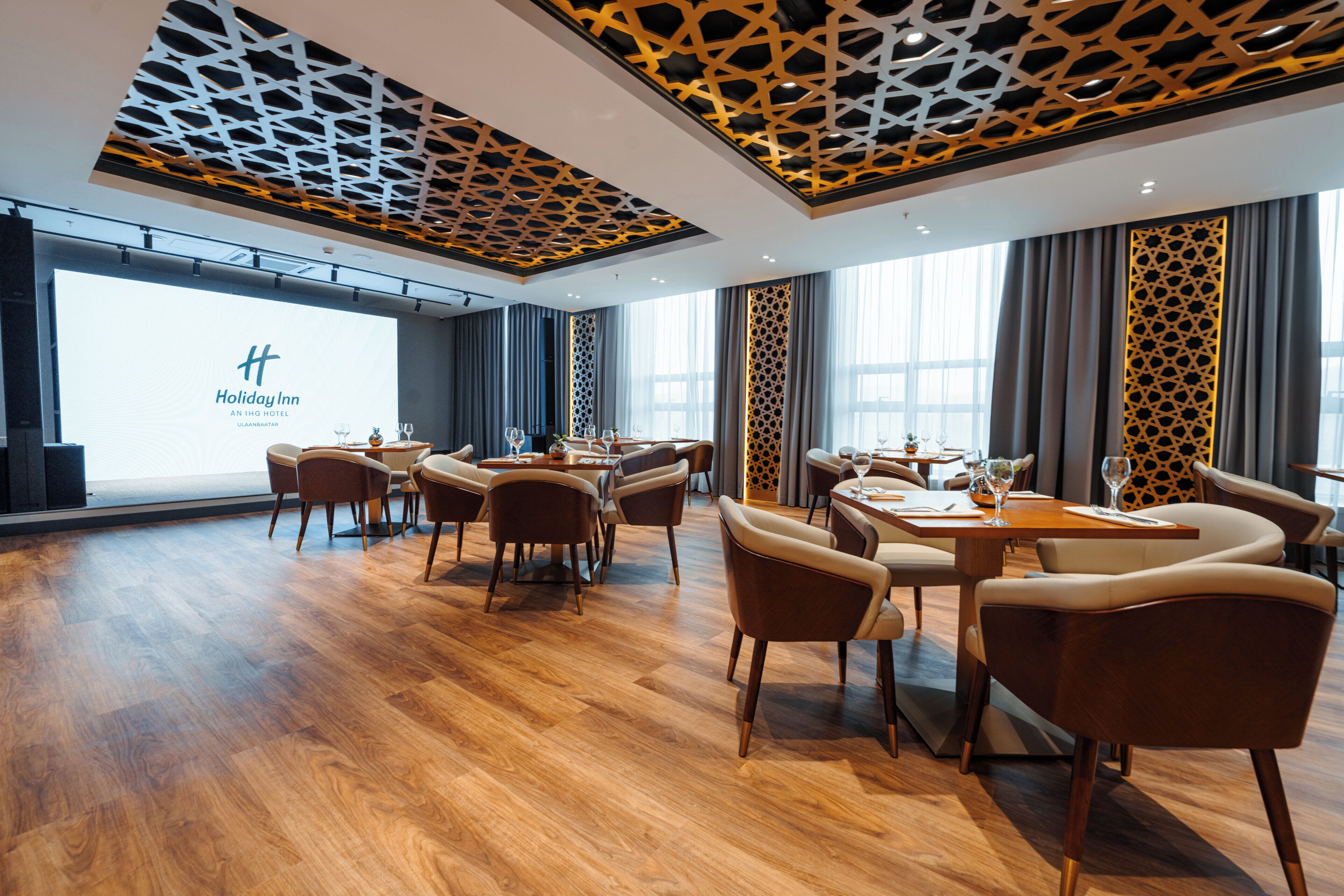 Ein Hotel-Essbereich mit Holzböden, moderner Einrichtung und einem großen Bildschirm, der den Namen des Hotels zeigt.