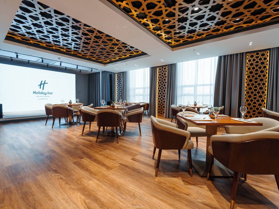 Ein Hotel-Essbereich mit Holzböden, moderner Einrichtung und einem großen Bildschirm, der den Namen des Hotels zeigt.