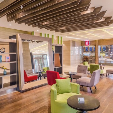 A modern lounge area with seating, a coffee shop in the background, and a wooden ceiling design.